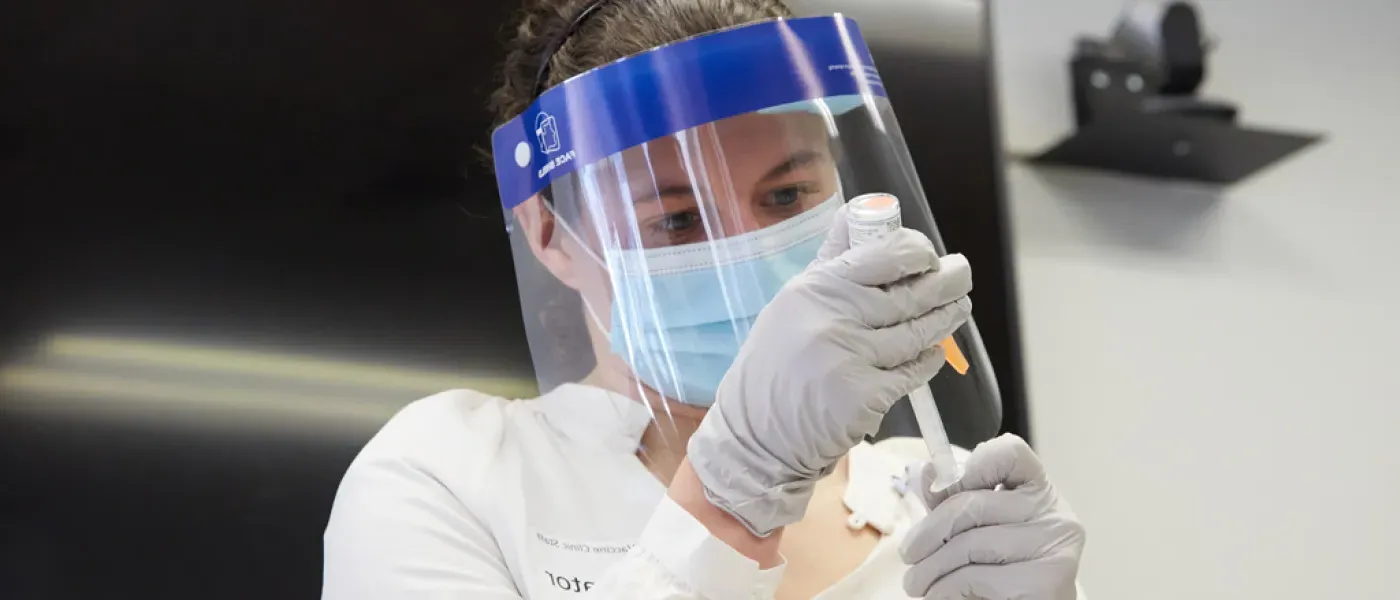 A U N E health professions student wearing P P E equipment is preparing a shot